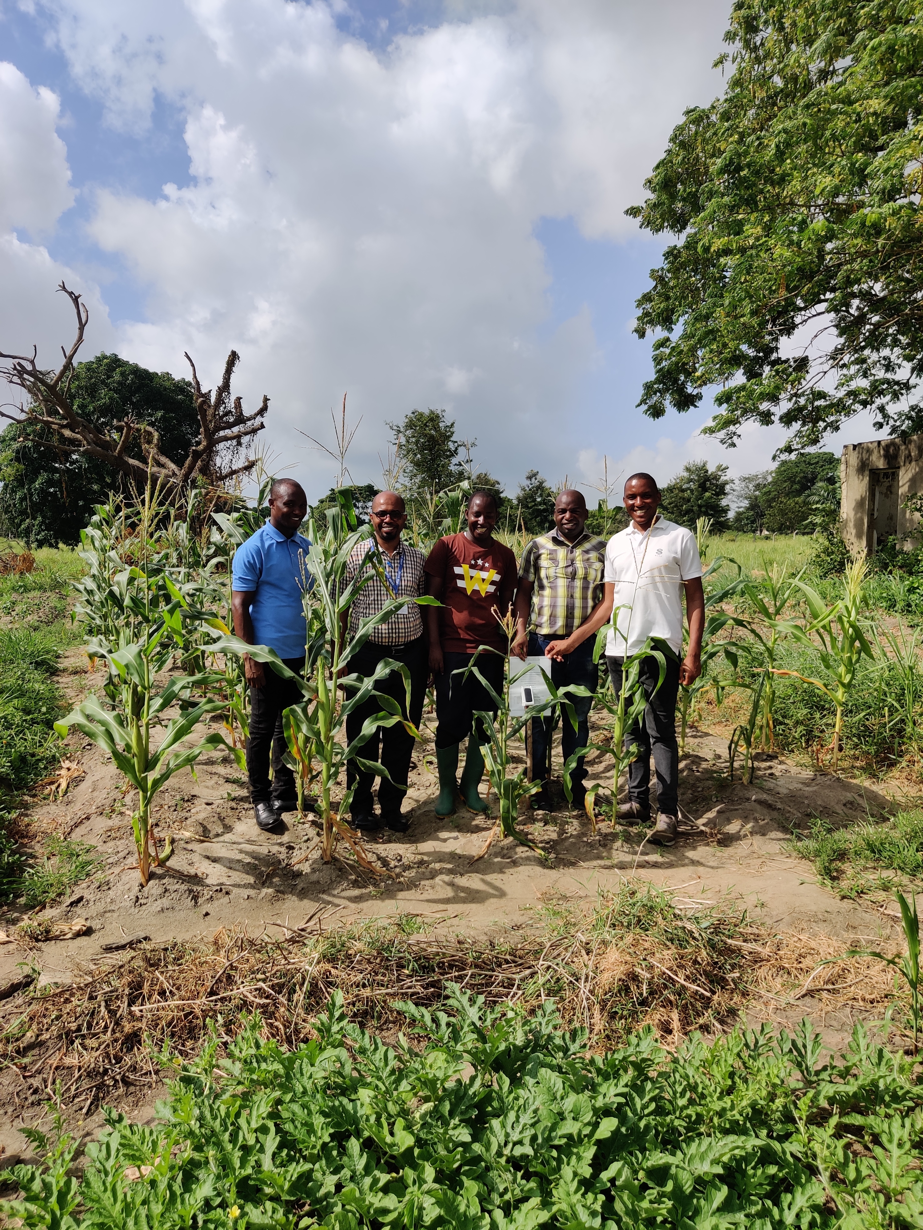 UDSM professors and agronomy staff standing behind a prototype weather station device.